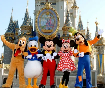 Disney characters pose in front of Cinderella Castle: Pluto, Donald Duck, Mickey Mouse, Minnie Mouse, Goofy.