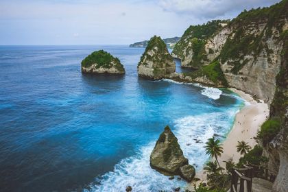 Rocky coastline with turquoise water, a sandy beach, and lush green cliffs.