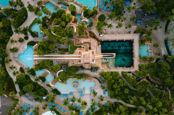 Overhead view of a resort with pools, water slides, buildings, and tropical landscaping. Turquoise water, green foliage.