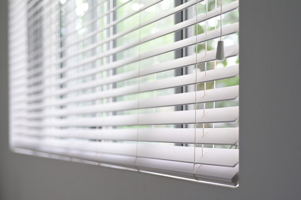 A Close Up Of A Window With White Blinds On It — Ron Ayton Curtains, Blinds & Shutters In Shelly Beach, NSW