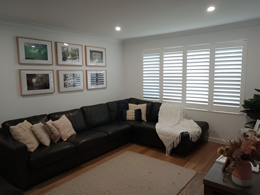 A Living Room With A Black Sectional Couch And White Shutters — Ron Ayton Curtains, Blinds & Shutters In Shelly Beach, NSW