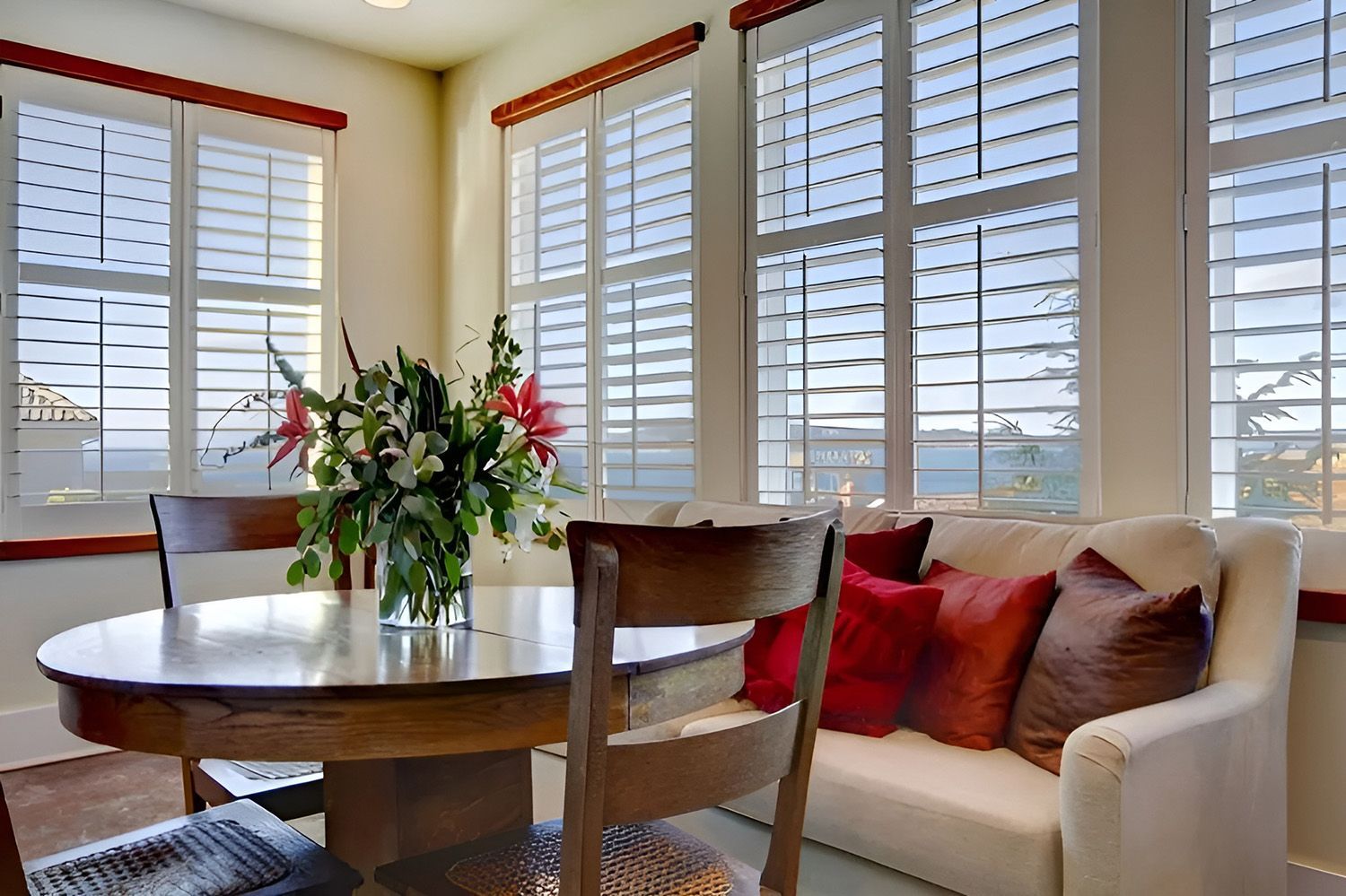 Dining Room with Window Seat with Red Pillows, with Window Shutters — Ron Ayton Curtains, Blinds & Shutters In Shelly Beach, NSW
