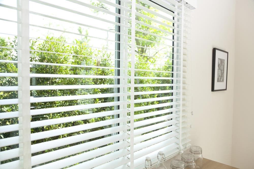 A Window With White Blinds And A Picture On The Wall — Ron Ayton Curtains, Blinds & Shutters In Shelly Beach, NSW