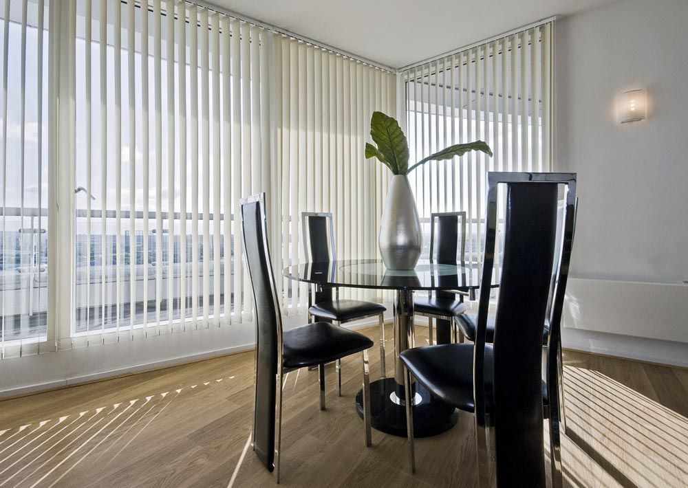 A Dining Room With A Table And Chairs And Vertical Blinds — Ron Ayton Curtains, Blinds & Shutters In Shelly Beach, NSW