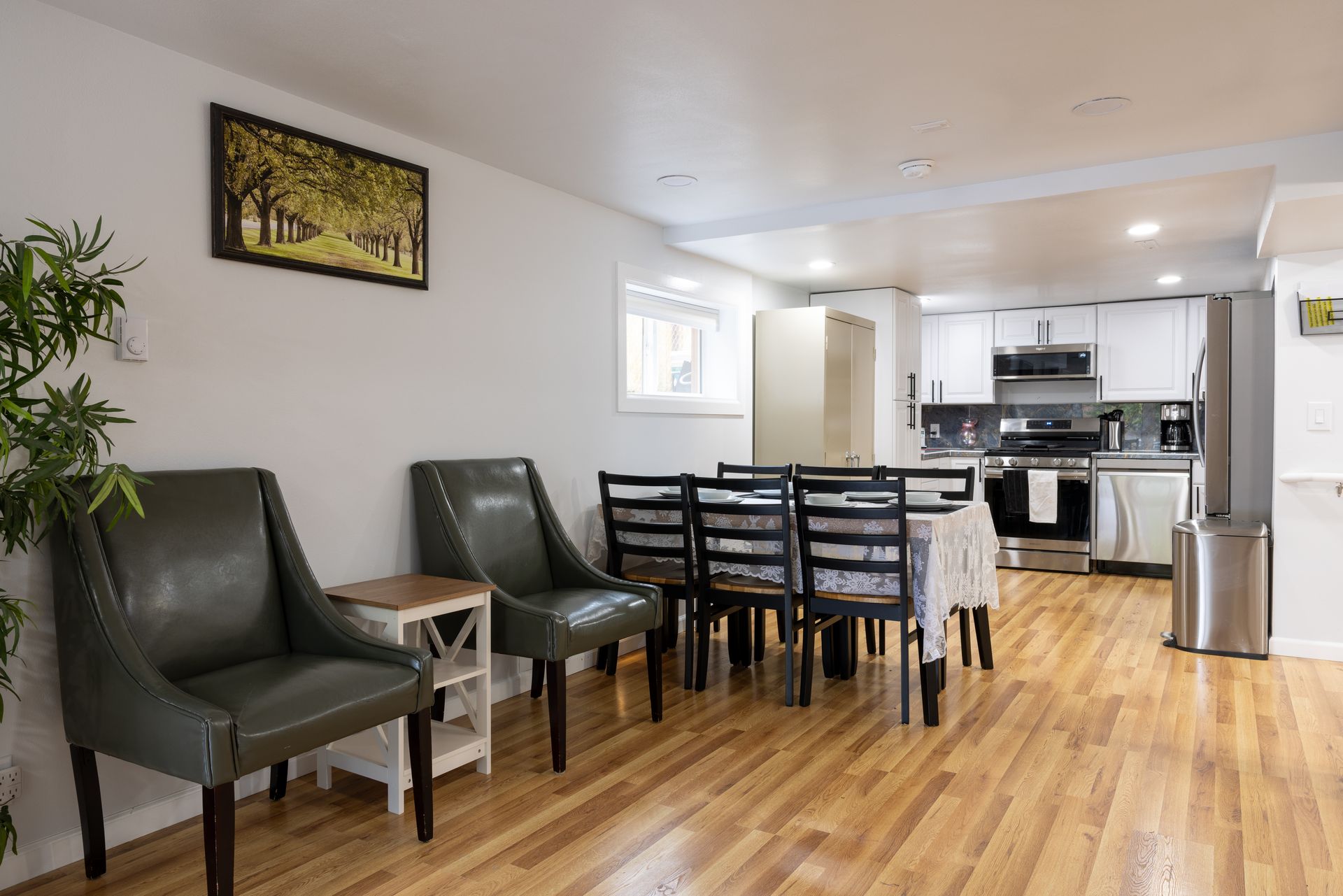 Spacious dining area with kitchen in the background. Green chairs, wooden table, and stainless steel appliances.