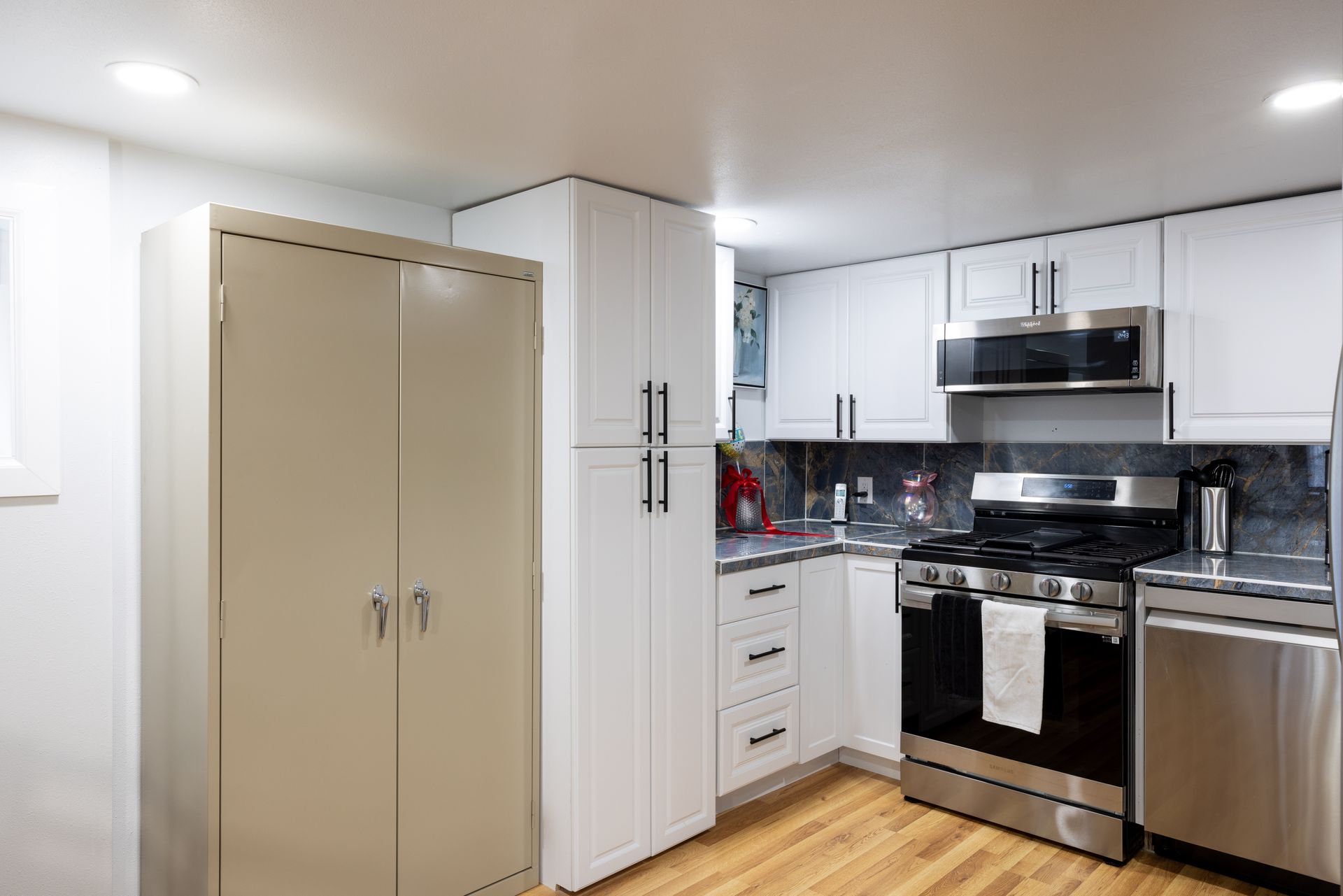 Small, modern kitchen with white cabinets, stainless steel appliances, and wood floor.