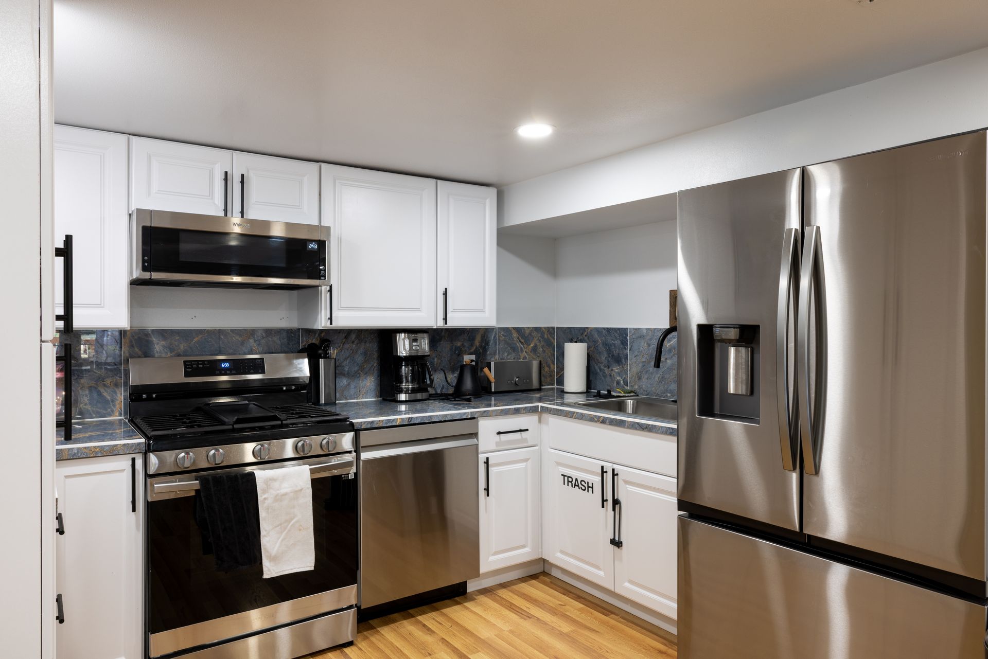Modern kitchen with white cabinets, stainless steel appliances, and dark countertops.