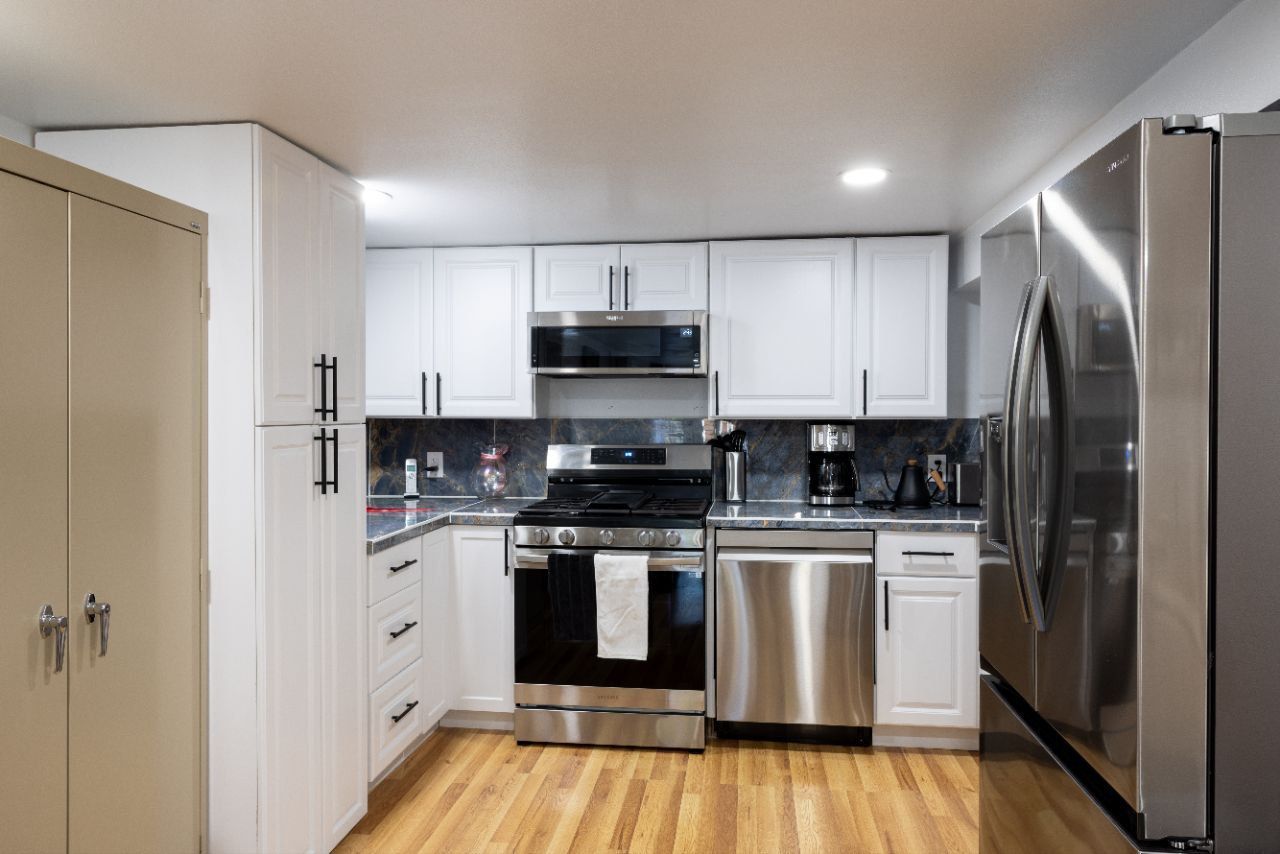White kitchen with stainless steel appliances and wooden floors.