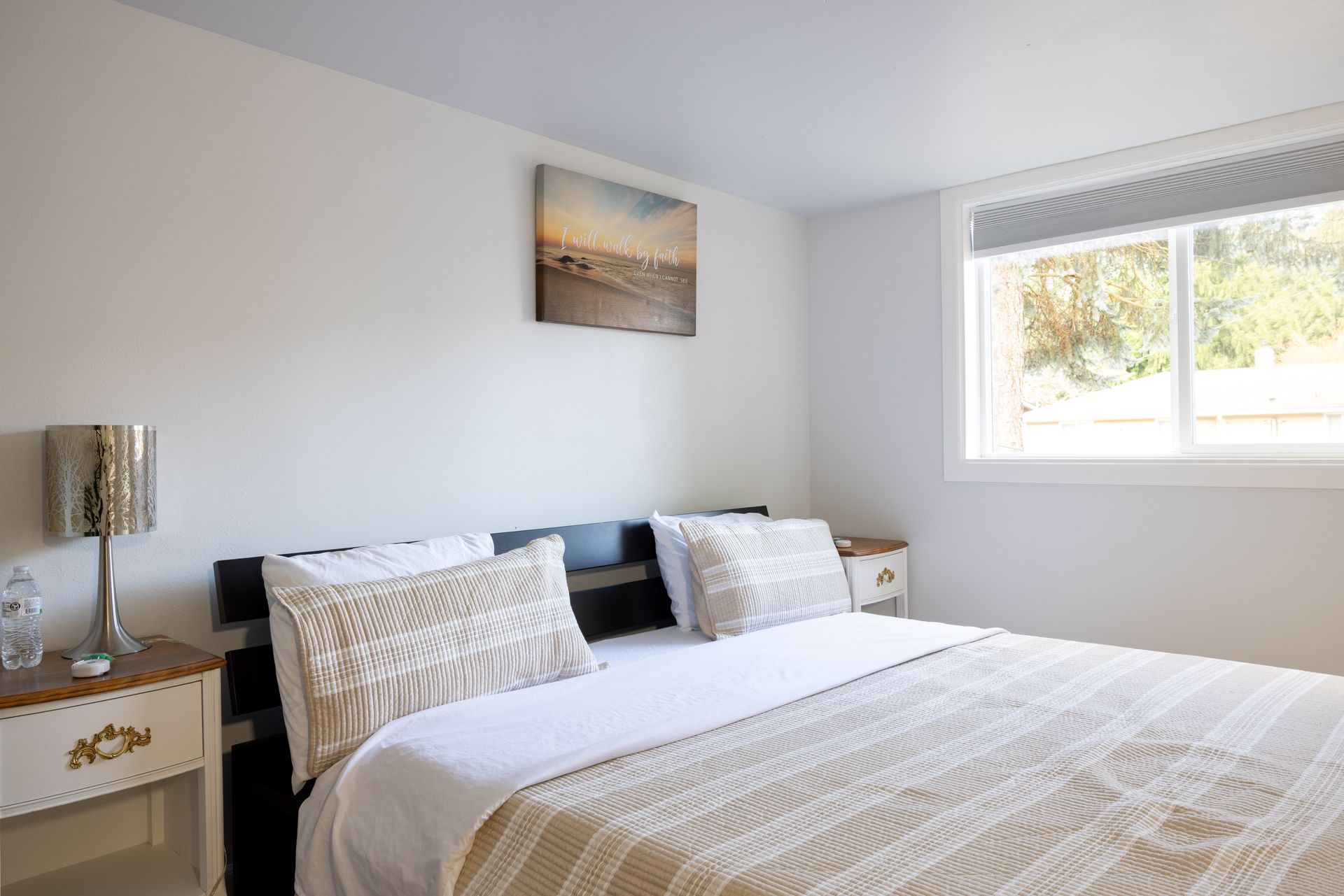 Bedroom with a bed, nightstands, window, and a small painting on the wall.