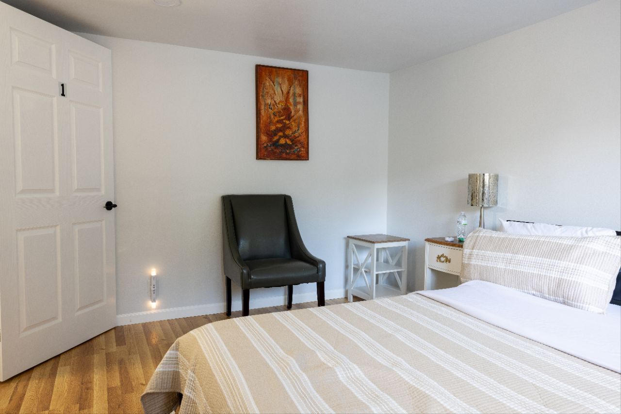 Bedroom with bed, chair, nightstand, art, and open white door.