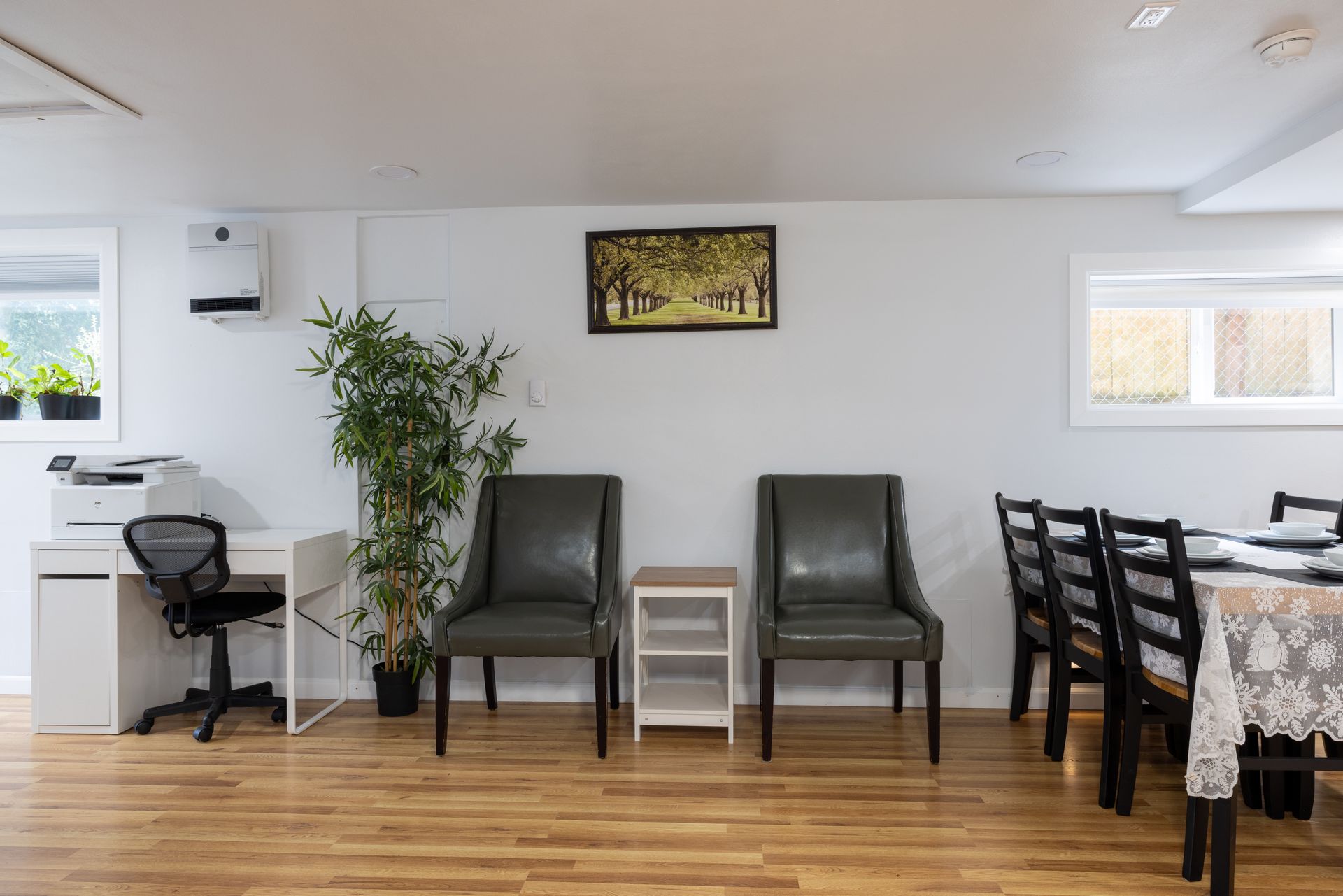 Office area with desk, chairs, artwork, and dining table set against a light-colored wall.