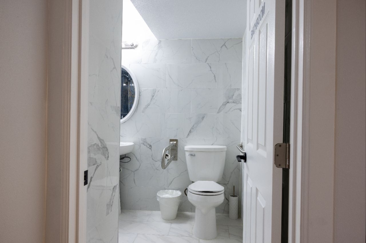 White bathroom with marble-look tiled walls, toilet, sink, and open door.
