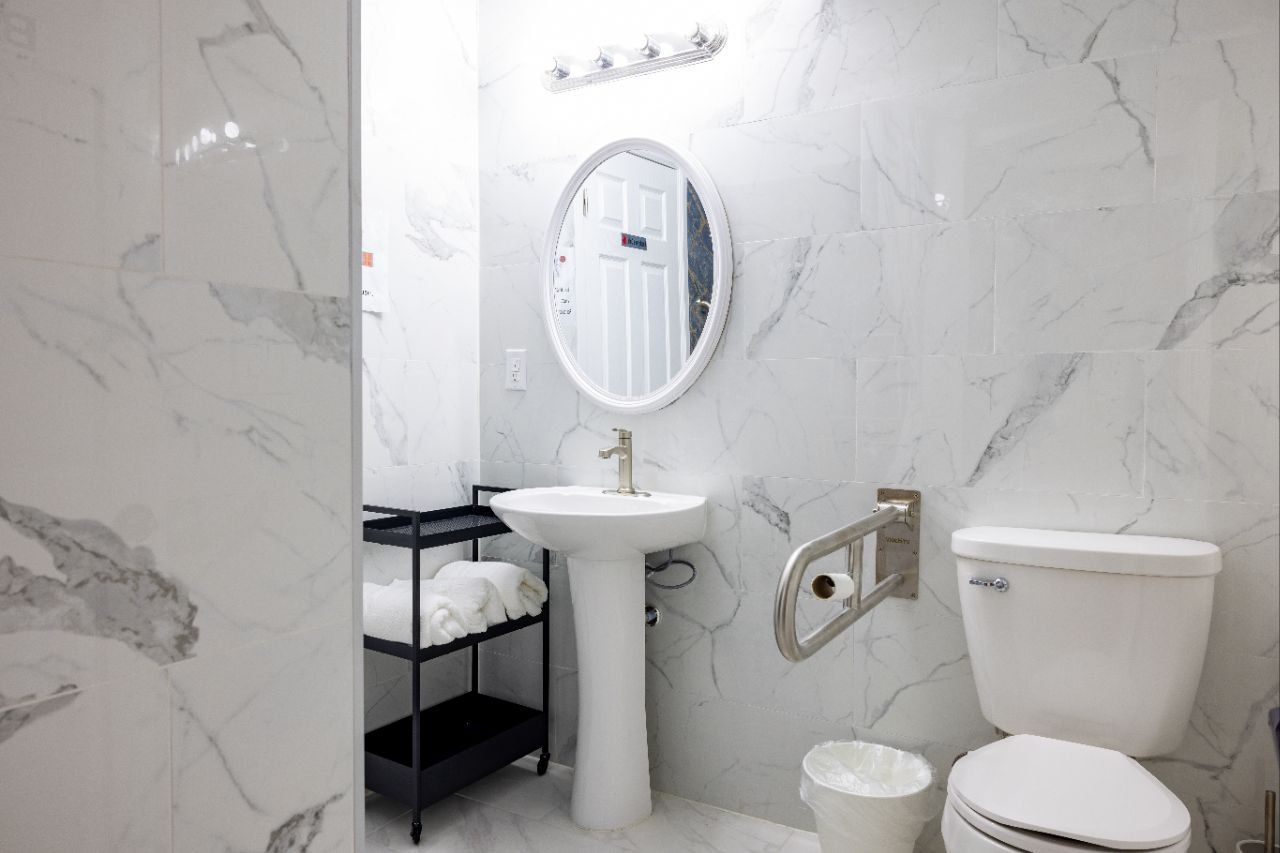 Bathroom with marble-patterned white walls, pedestal sink, toilet, and grab bar for accessibility.