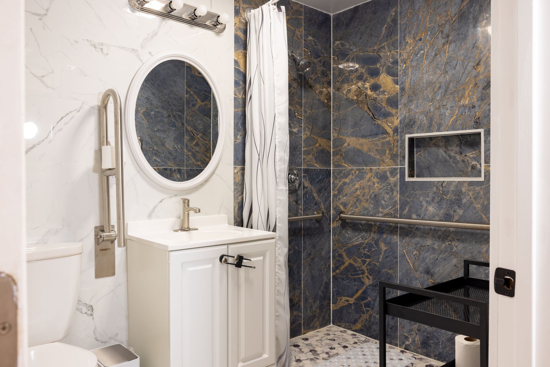 Bathroom with accessible features: shower, grab bars, toilet, and vanity. Marble walls and flooring.