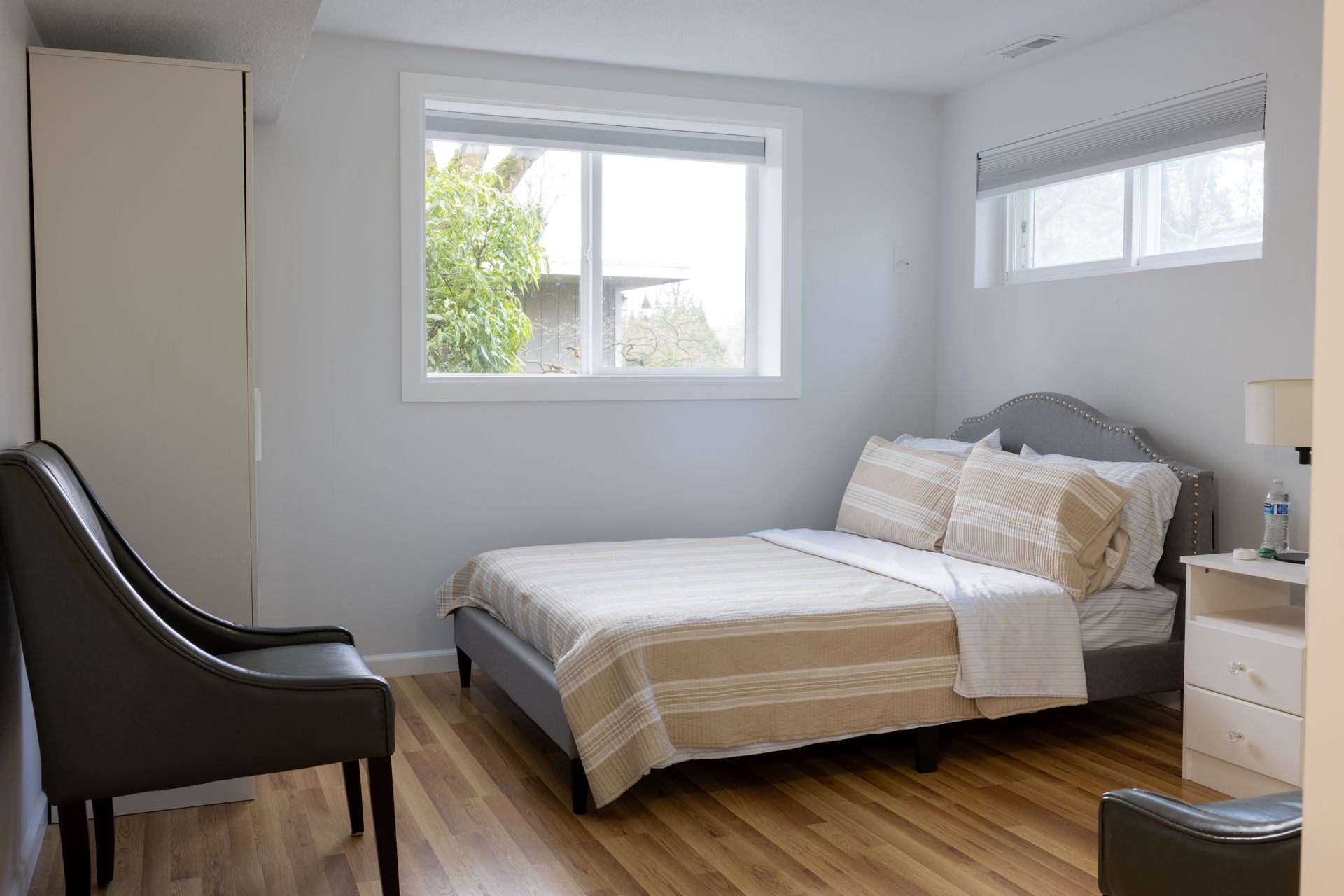 Bedroom with a bed, small nightstand, two windows, two chairs, and a closet.