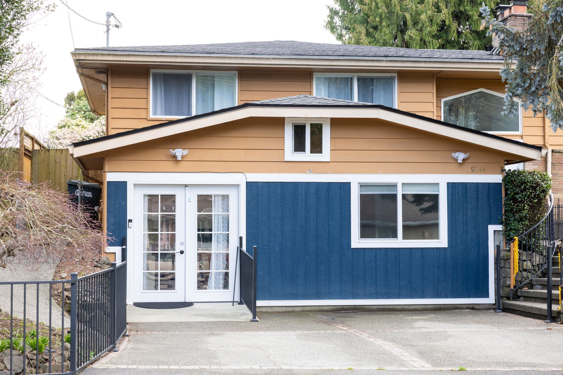 Two-story house with blue and tan siding, white trim, and a small front yard with a gate.