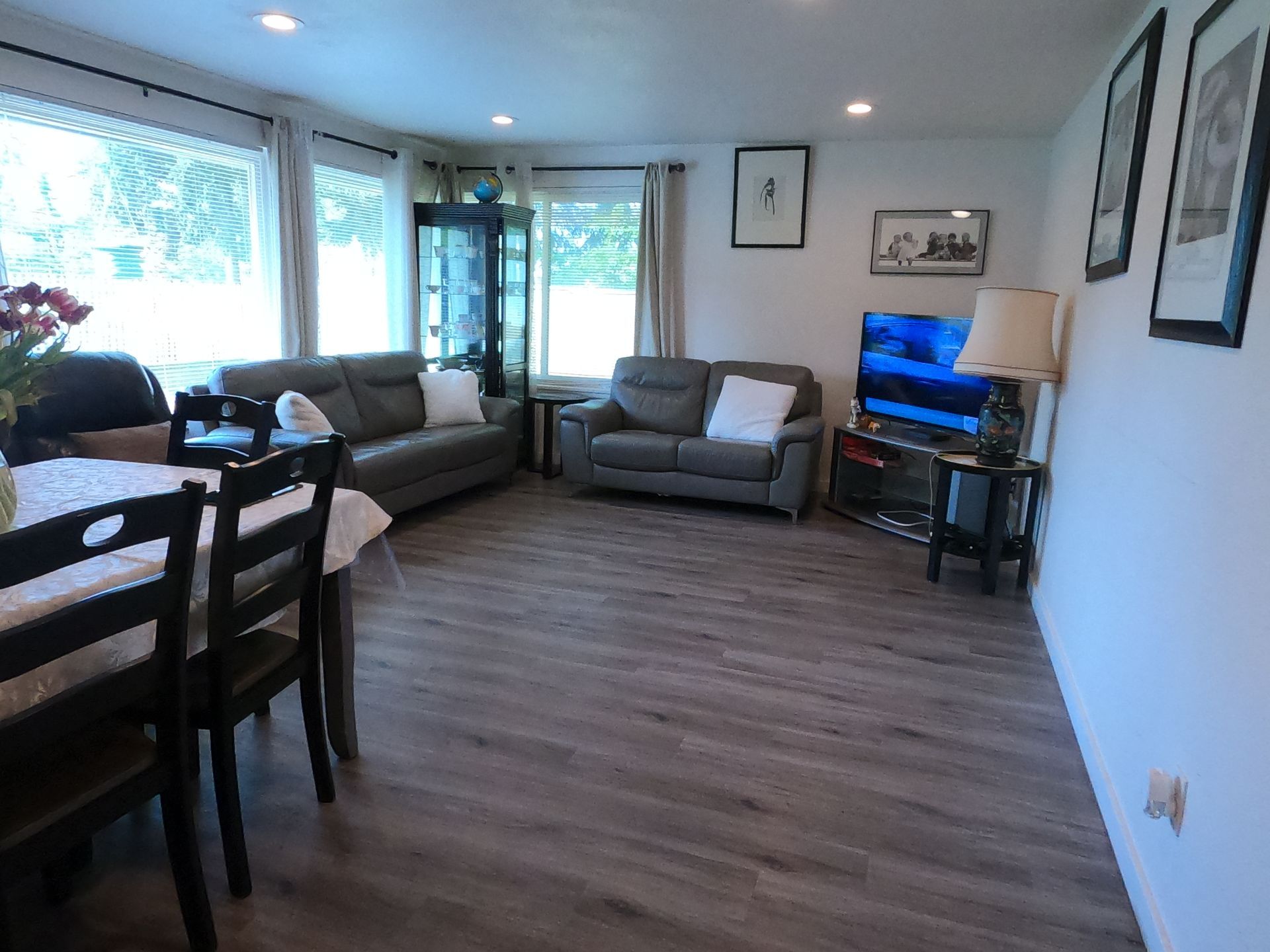 Living room with gray sofas, TV, dining table, and large windows.