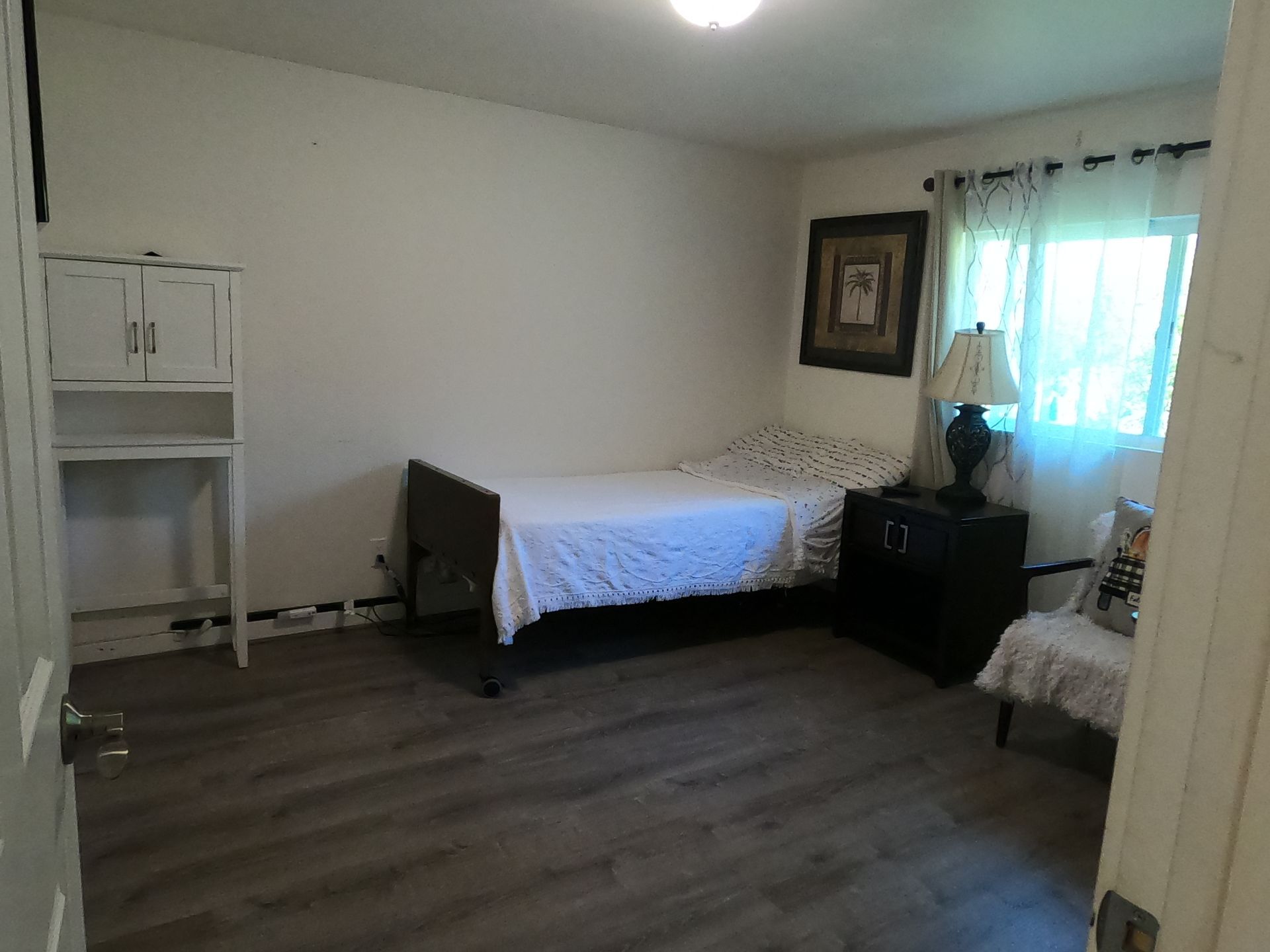 Bedroom with bed, nightstand, cabinet, and chair; natural light through window.