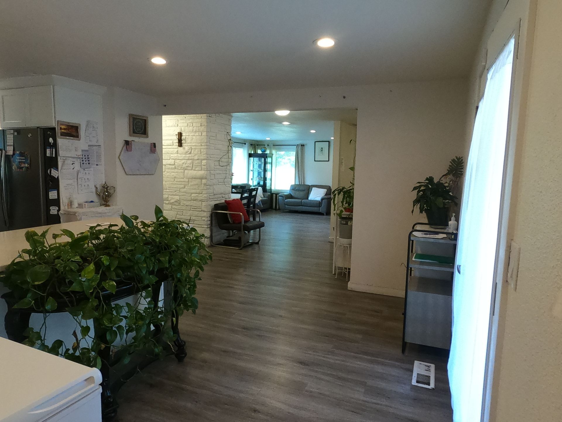 Interior view: Open floor plan with a kitchen, dining area, and living room. Green plants and gray flooring.