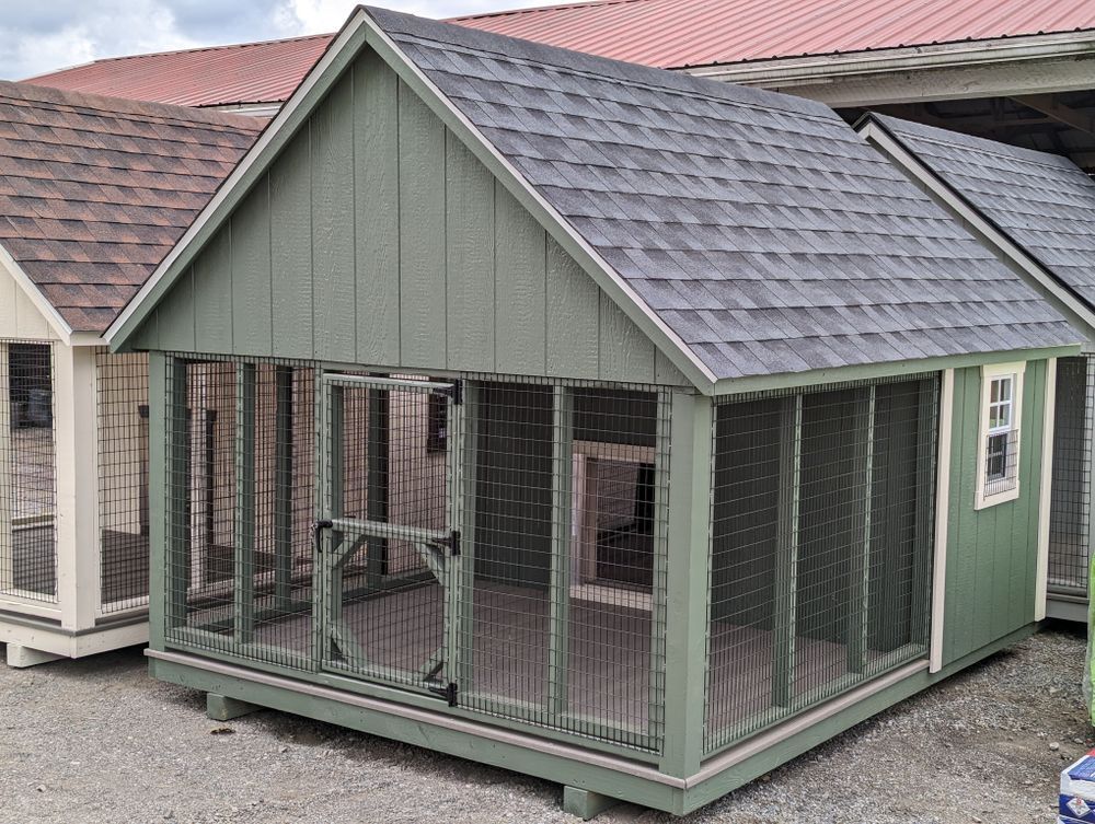 A green dog kennel with a gray roof is sitting in front of a building.