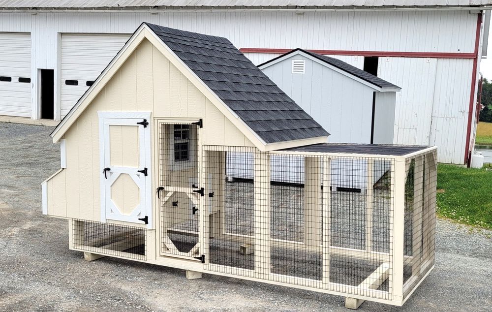 A chicken coop with a black roof is sitting in front of a white barn