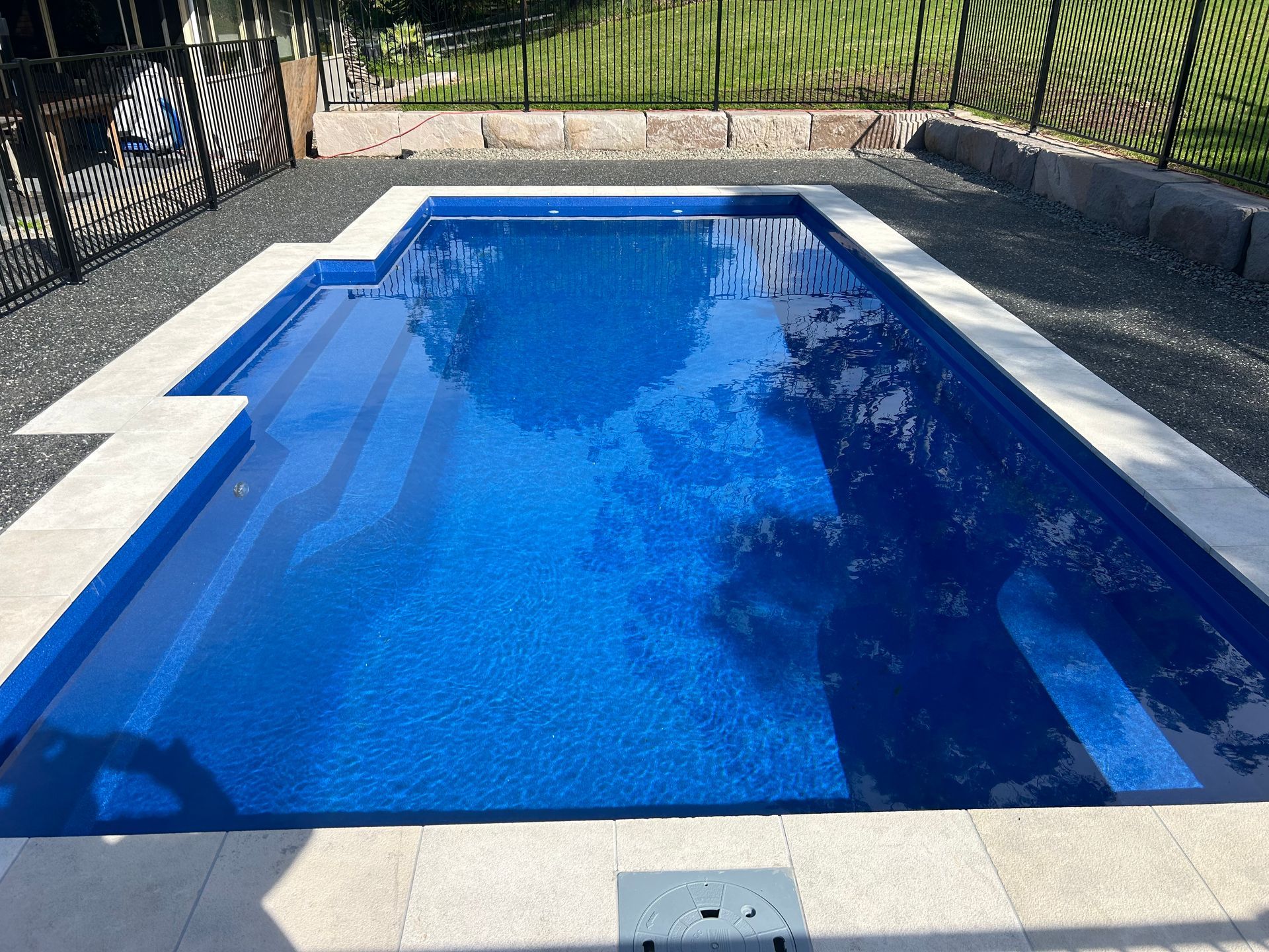 A large blue swimming pool is surrounded by a fence. — Steve Merrick Family Swimming Pools in Failford, NSW