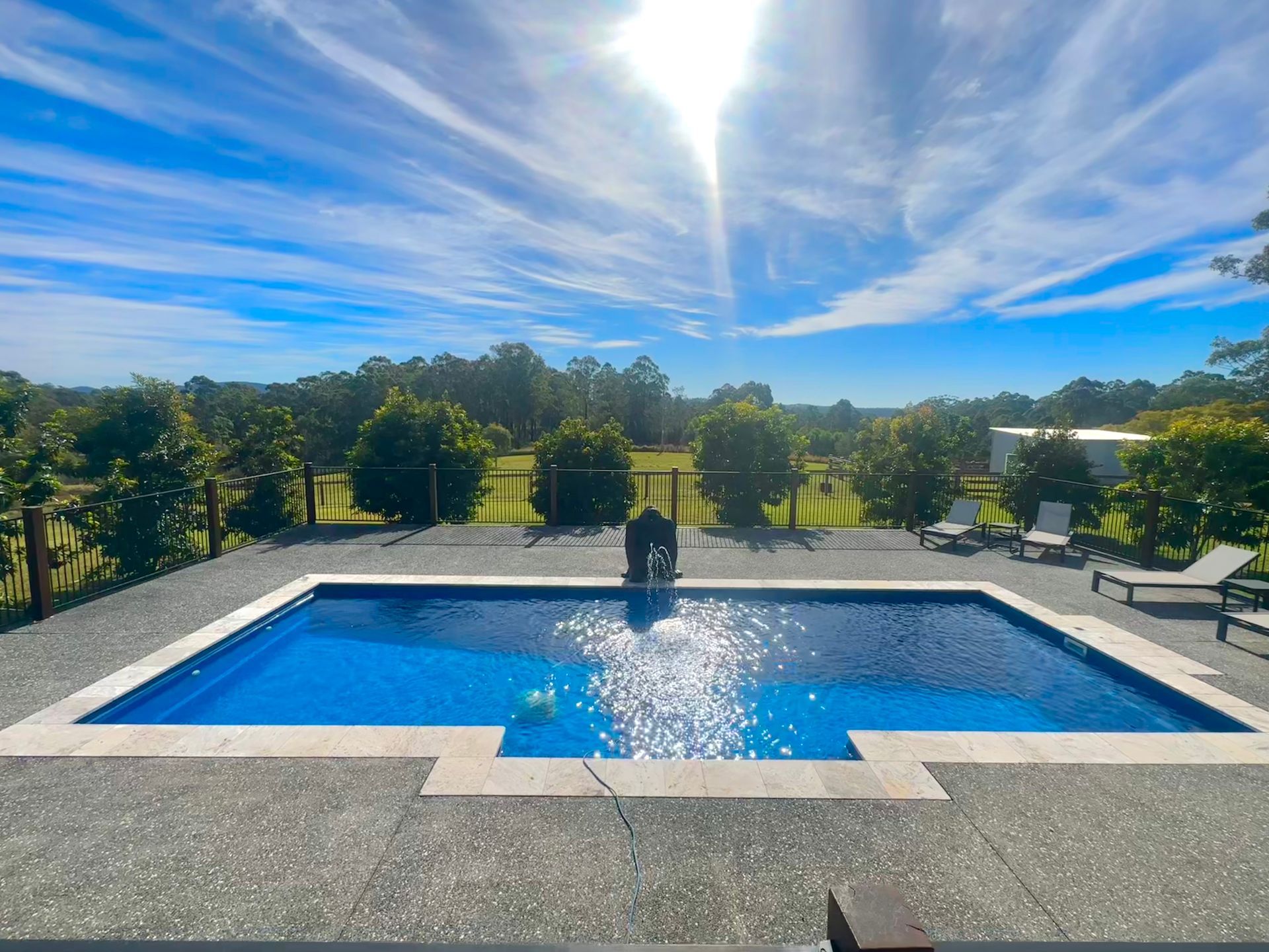 A large swimming pool is surrounded by chairs and trees on a sunny day — Steve Merrick Family Swimming Pools in Taree, NSW