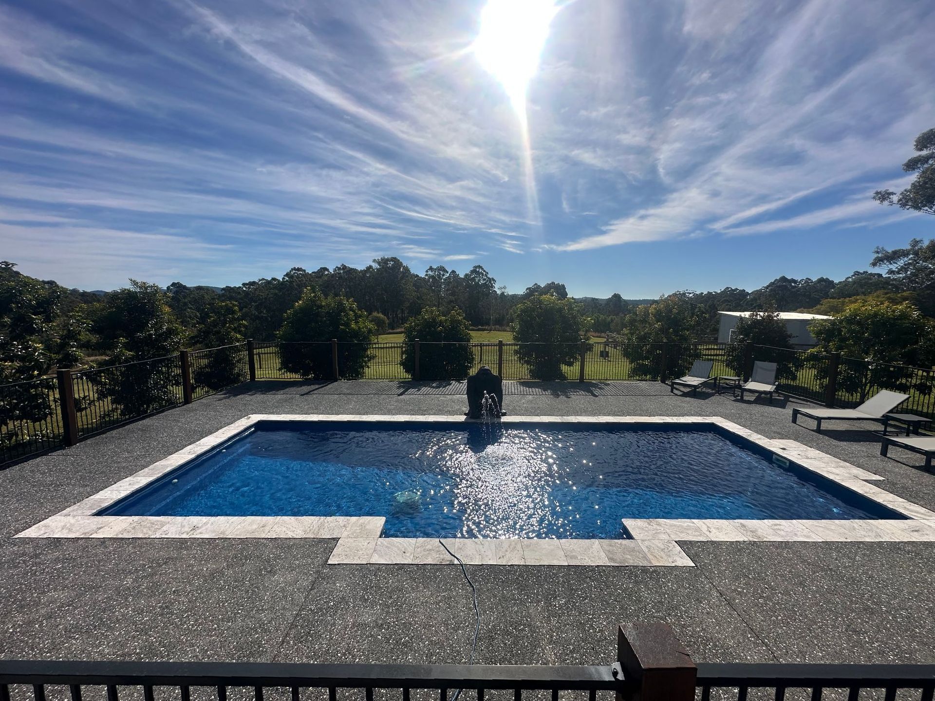 A large swimming pool surrounded by chairs and trees on a sunny day — Steve Merrick Family Swimming Pools in Pacific Palms, NSW