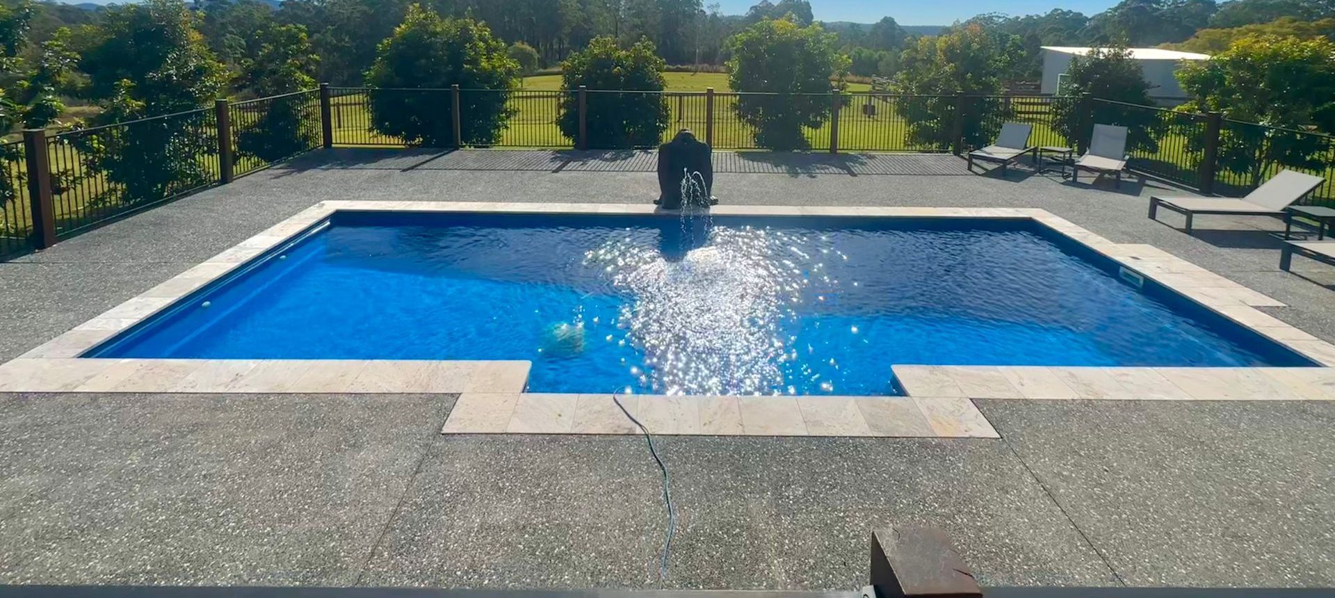 A Large Swimming Pool With a Glass Fence Around It — Steve Merrick Family Swimming Pools in Nabiac, NSW