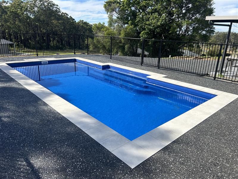 A large swimming pool surrounded by a fence and trees. — Steve Merrick Family Swimming Pools in Old Bar, NSW