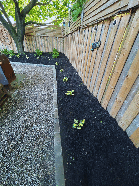 A wooden fence is surrounded by gravel and black mulch.
