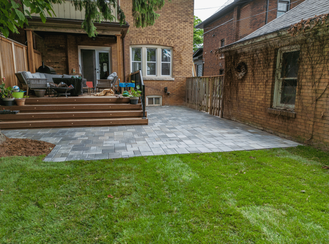 A backyard with a patio and a deck in front of a brick house.