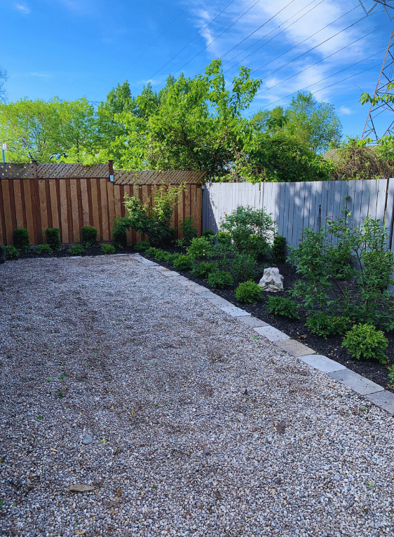 A gravel driveway leading to a wooden fence with trees in the background.
