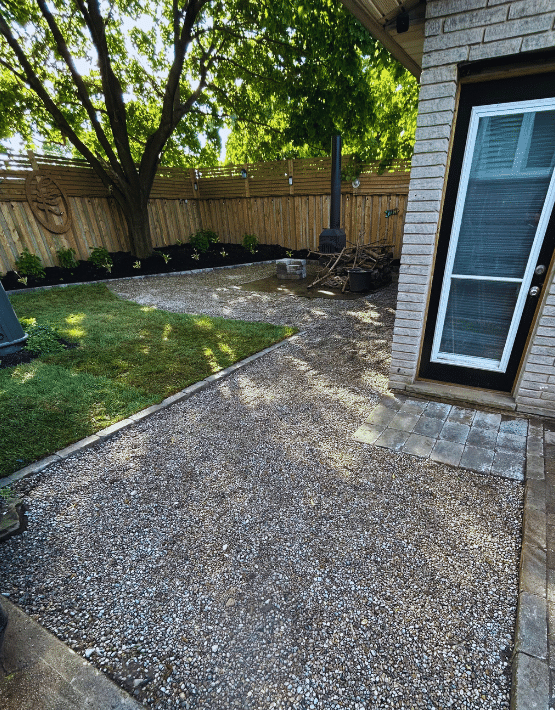A brick house with a gravel driveway and a fence in the backyard.