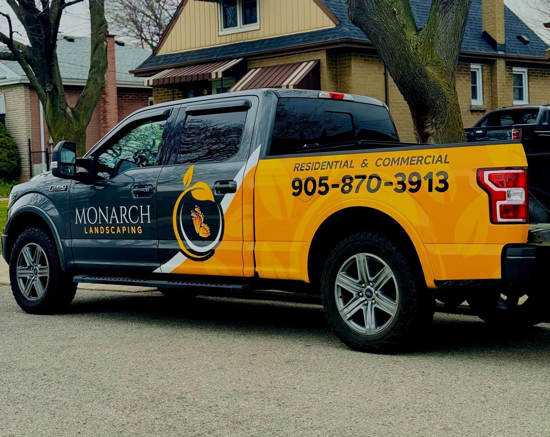 A yellow truck with monarch written on the back is parked in front of a house