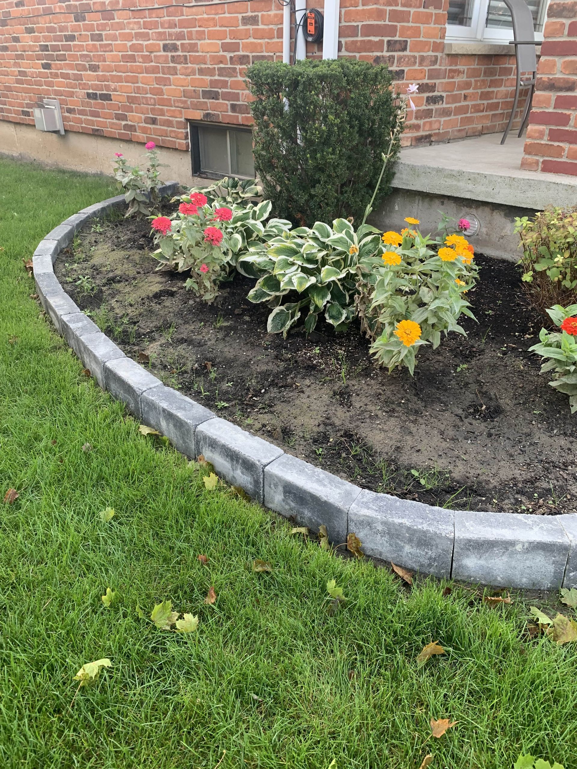 A garden with flowers and a curb in front of a brick house.