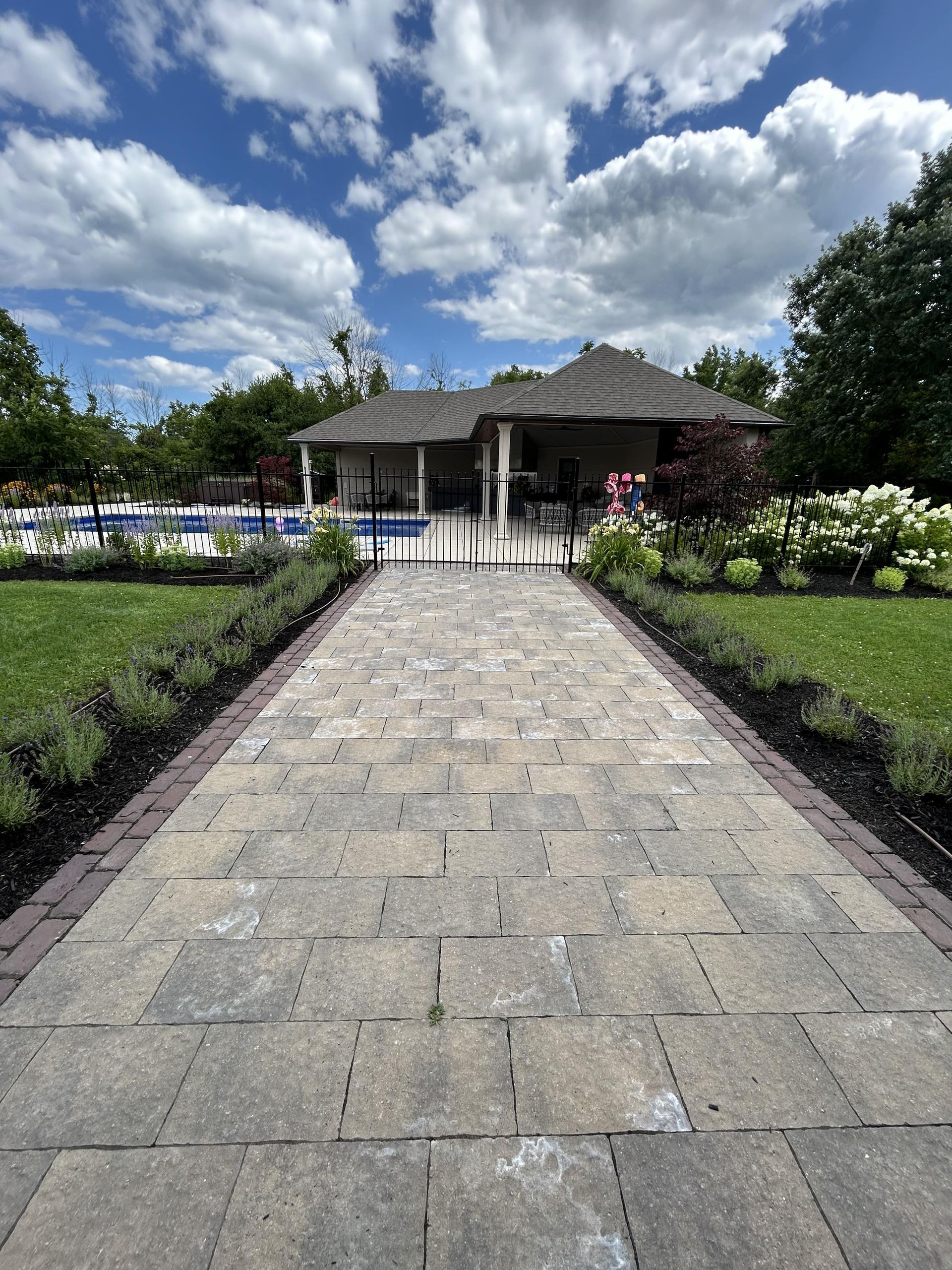 A brick walkway leading to a house with a pool in the background.