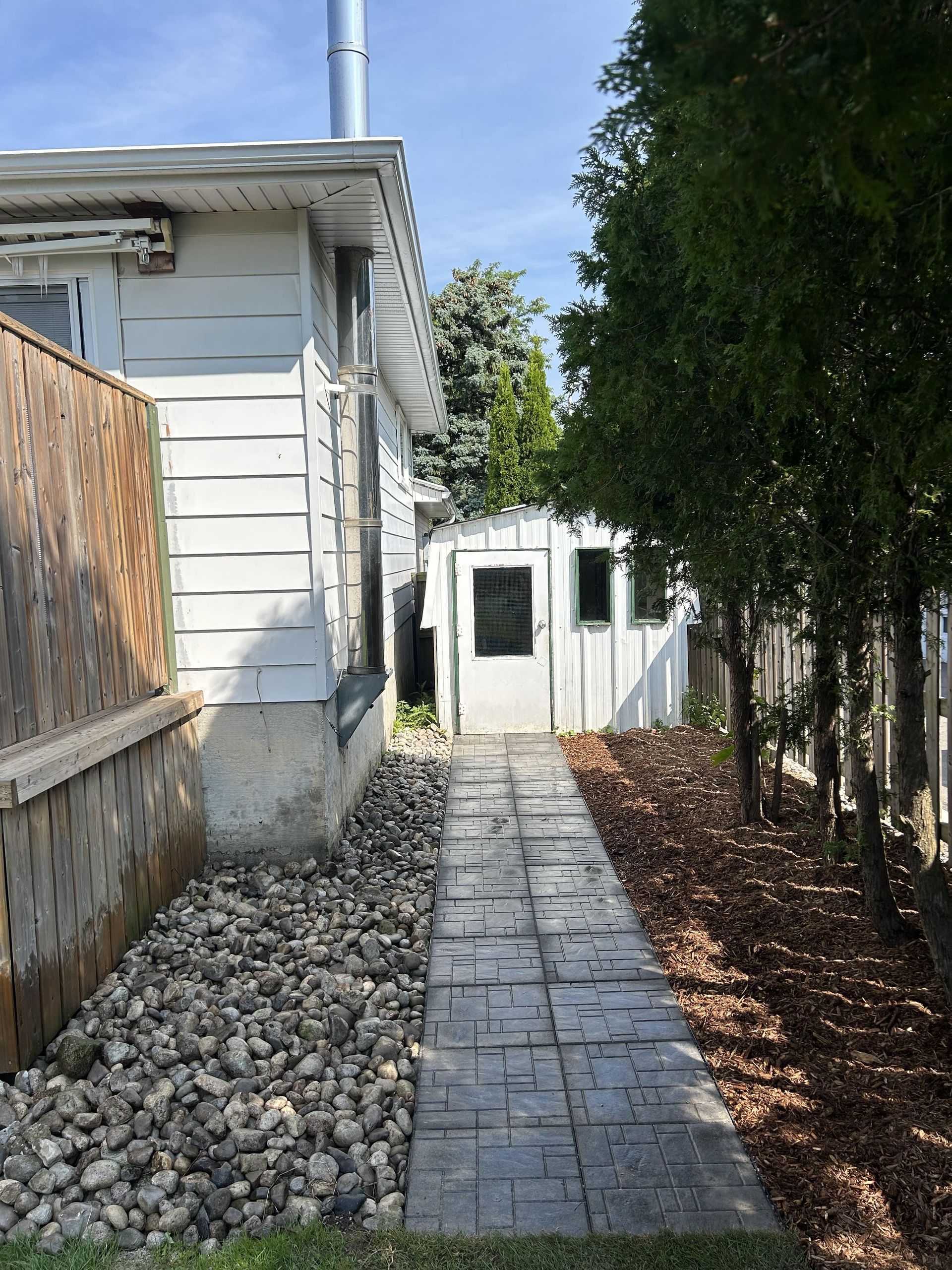 A walkway leading to a white house with a shed in the backyard.