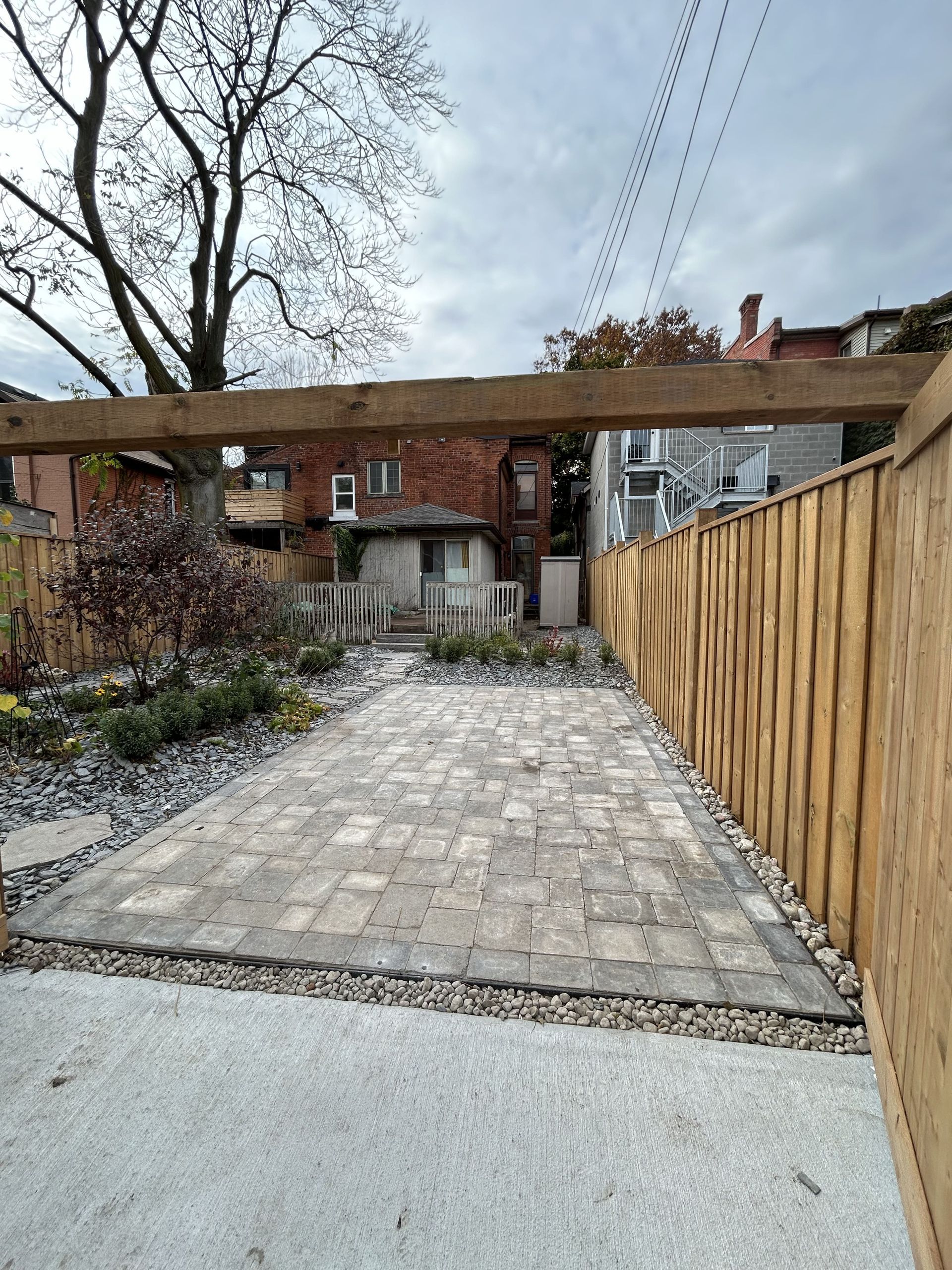 A wooden fence surrounds a brick driveway leading to a house.