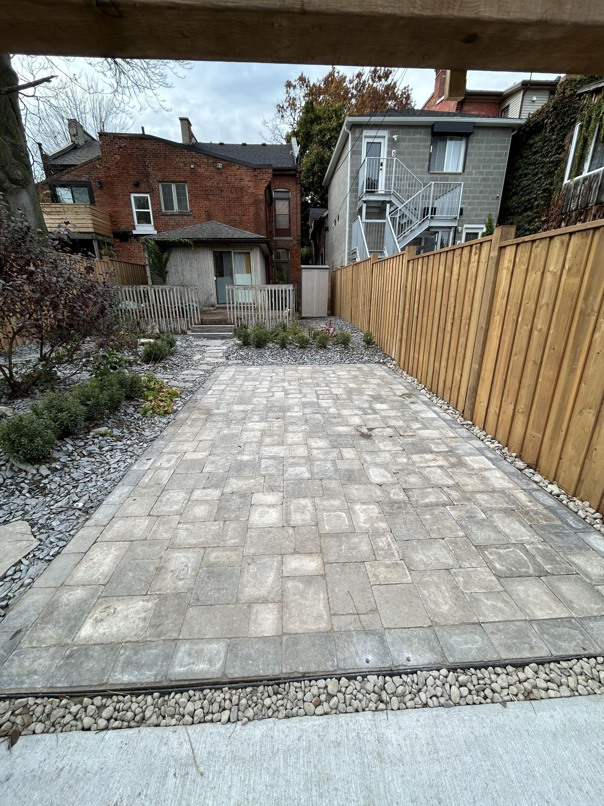 A brick walkway leading to a house with a wooden fence.