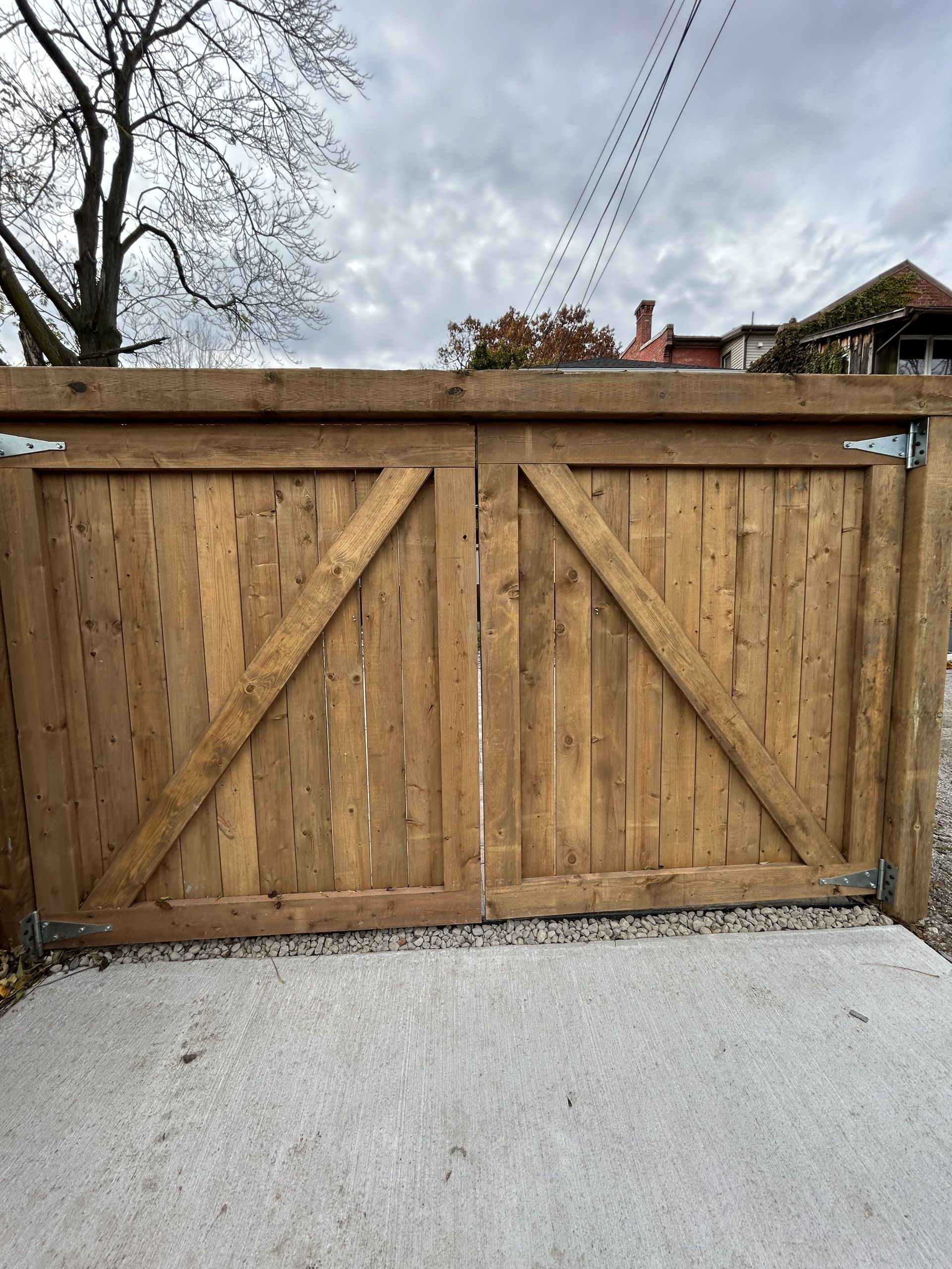 A wooden gate is sitting on top of a gravel driveway.