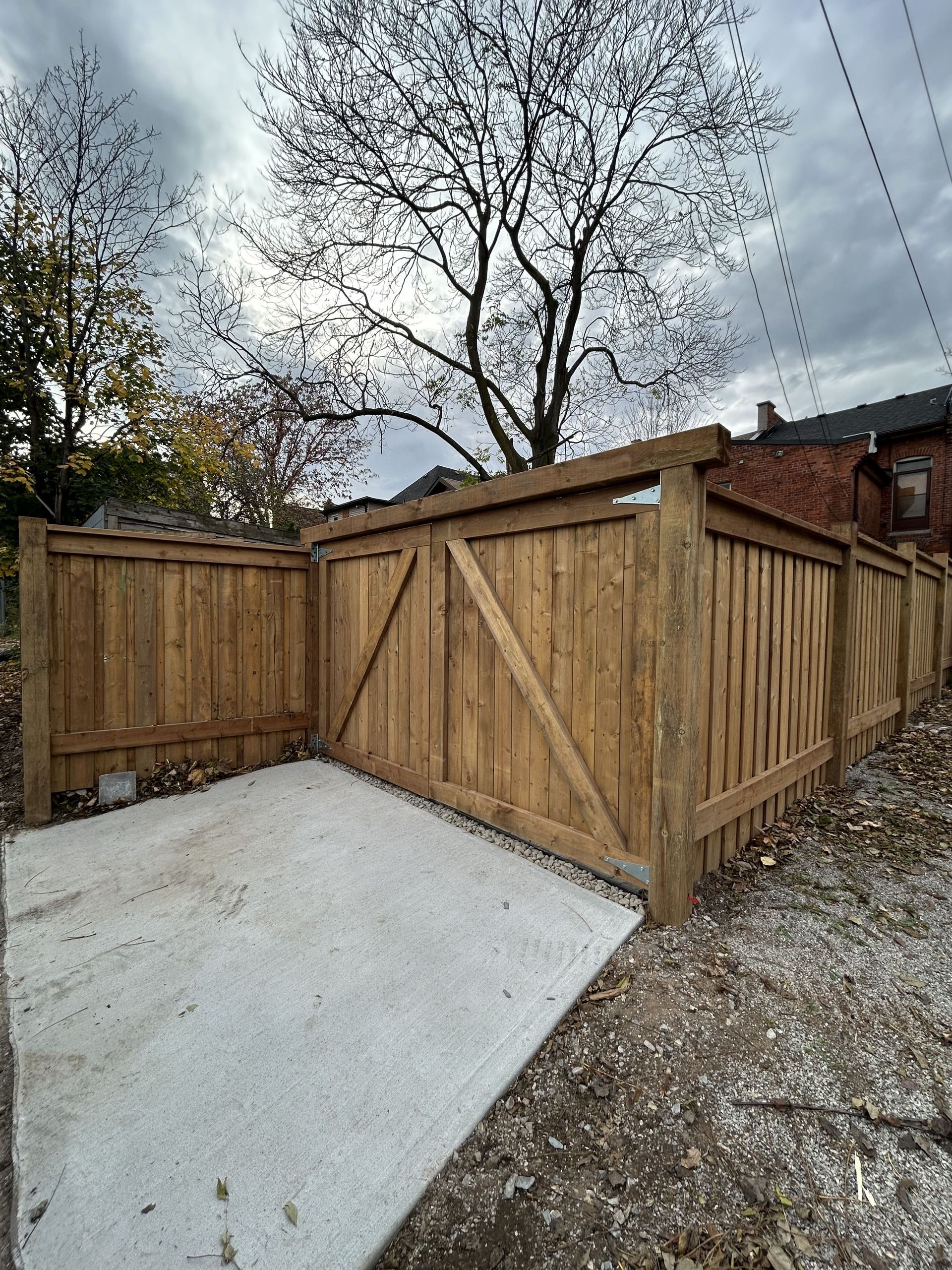 A wooden fence surrounds a concrete driveway in a backyard.