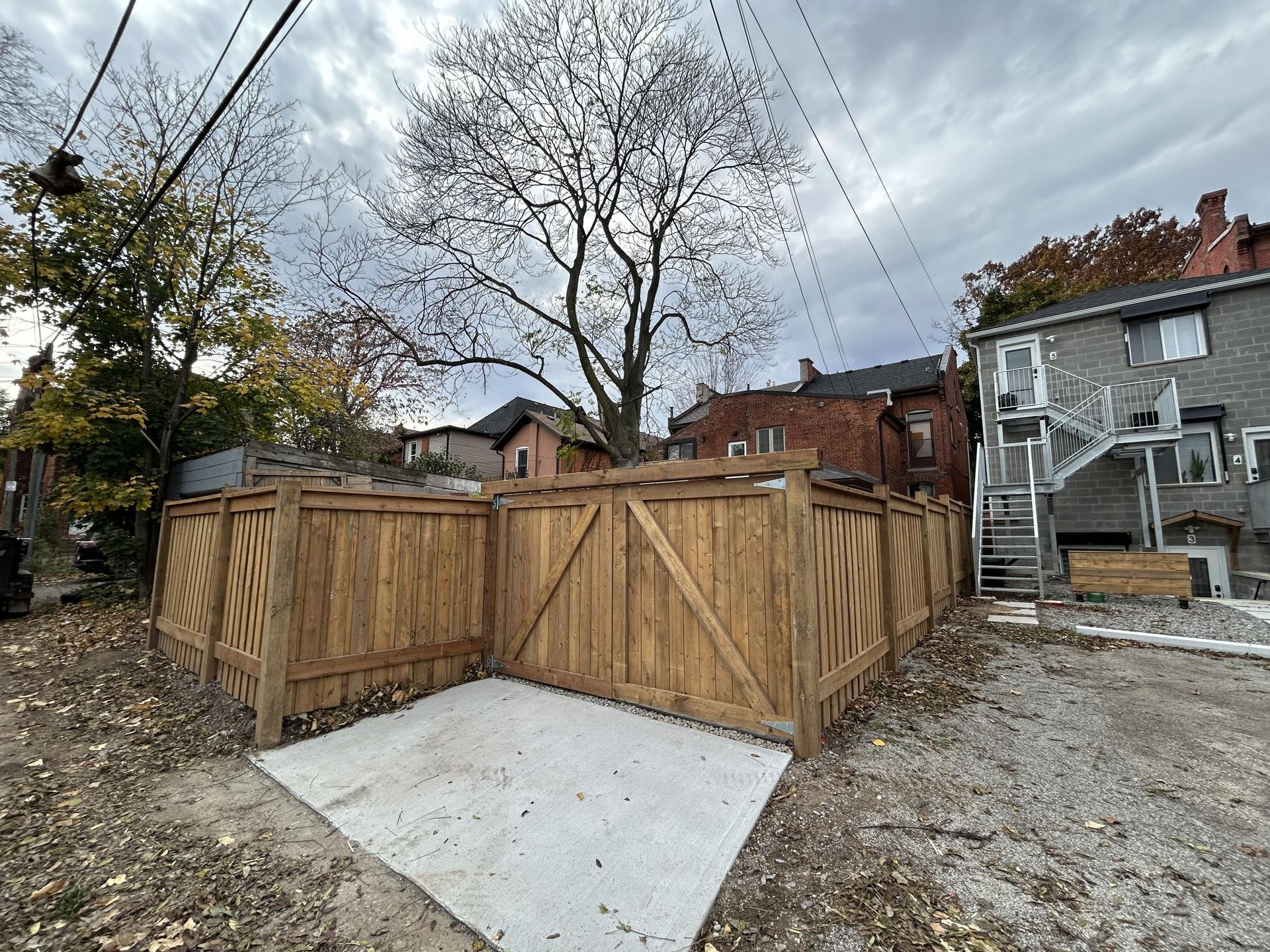 A wooden fence is surrounding a concrete area in a backyard.