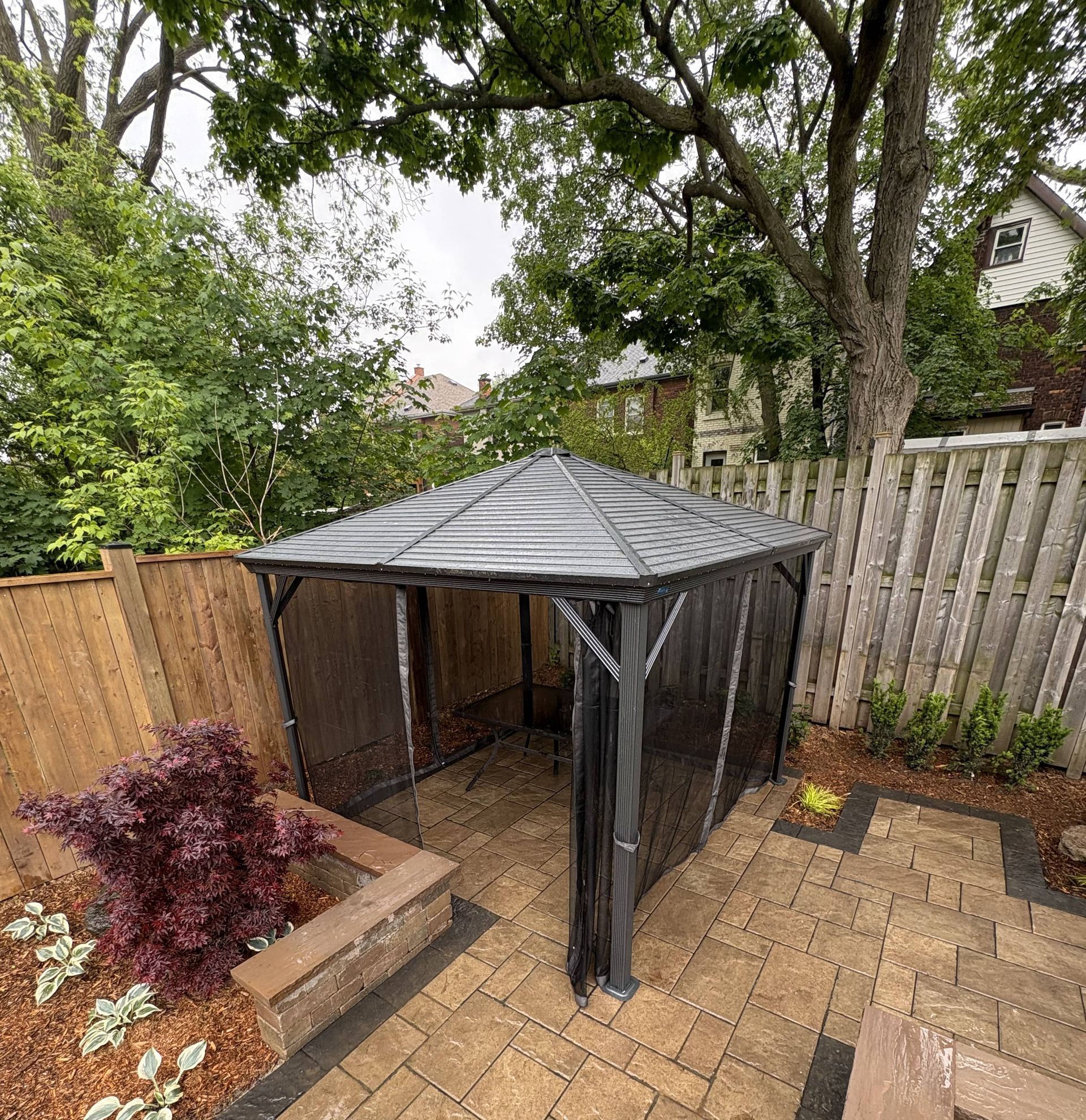 A gazebo is sitting on top of a brick patio next to a wooden fence.