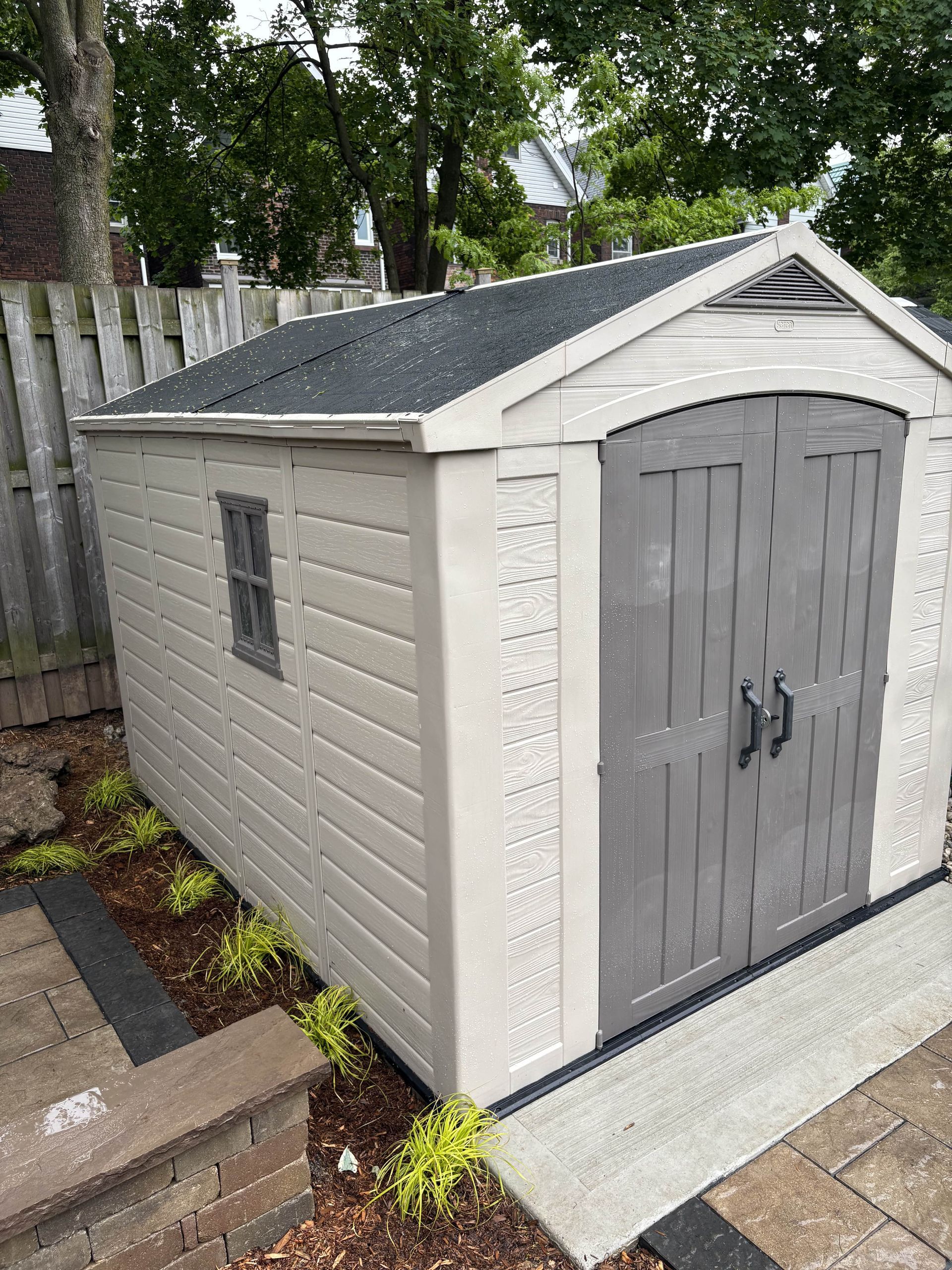A white plastic shed with a black roof is sitting in a backyard.