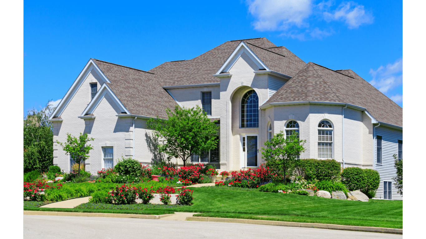 A large white house with a brown roof is sitting on top of a lush green hillside.