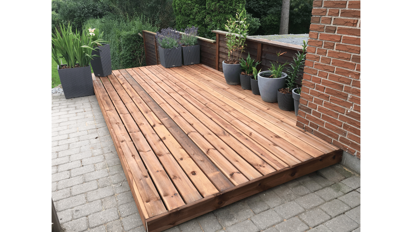 A wooden deck with potted plants on it next to a brick wall.