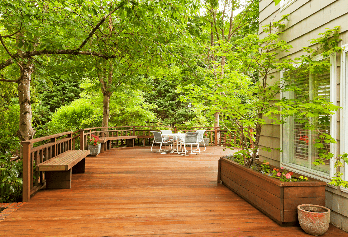 A wooden deck with a bench and a planter in front of a house.