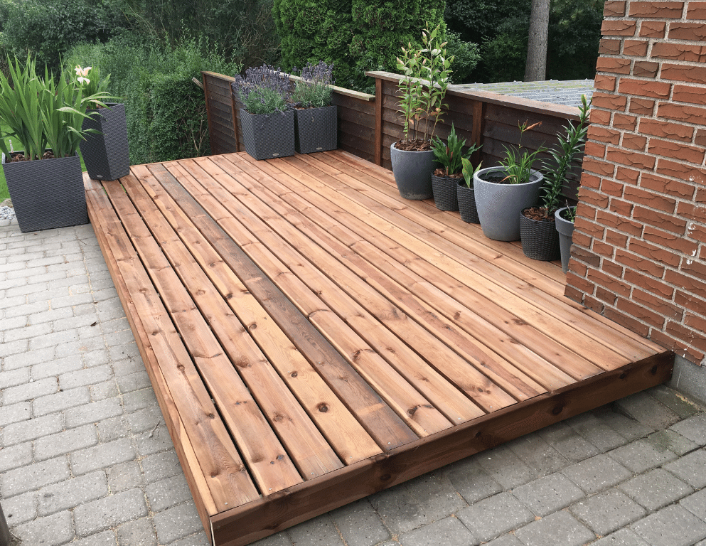 A wooden deck with potted plants on it in front of a brick building