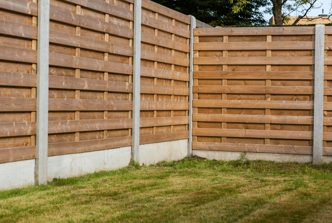 A wooden fence surrounds a lush green lawn in a backyard.